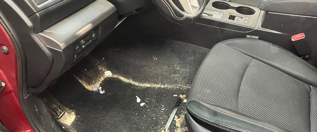 A car footwell before cleaning, with dirt worked into the carpet